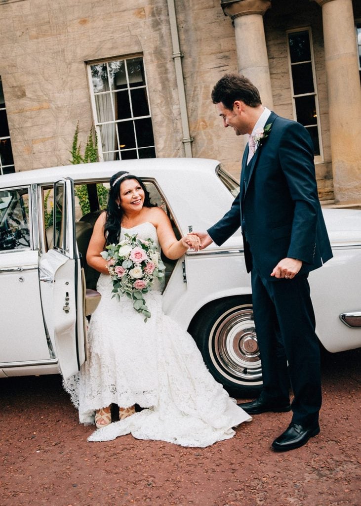 Groom helping bride from their Rolls-Royce in front of Linden Hall in Northumberland
