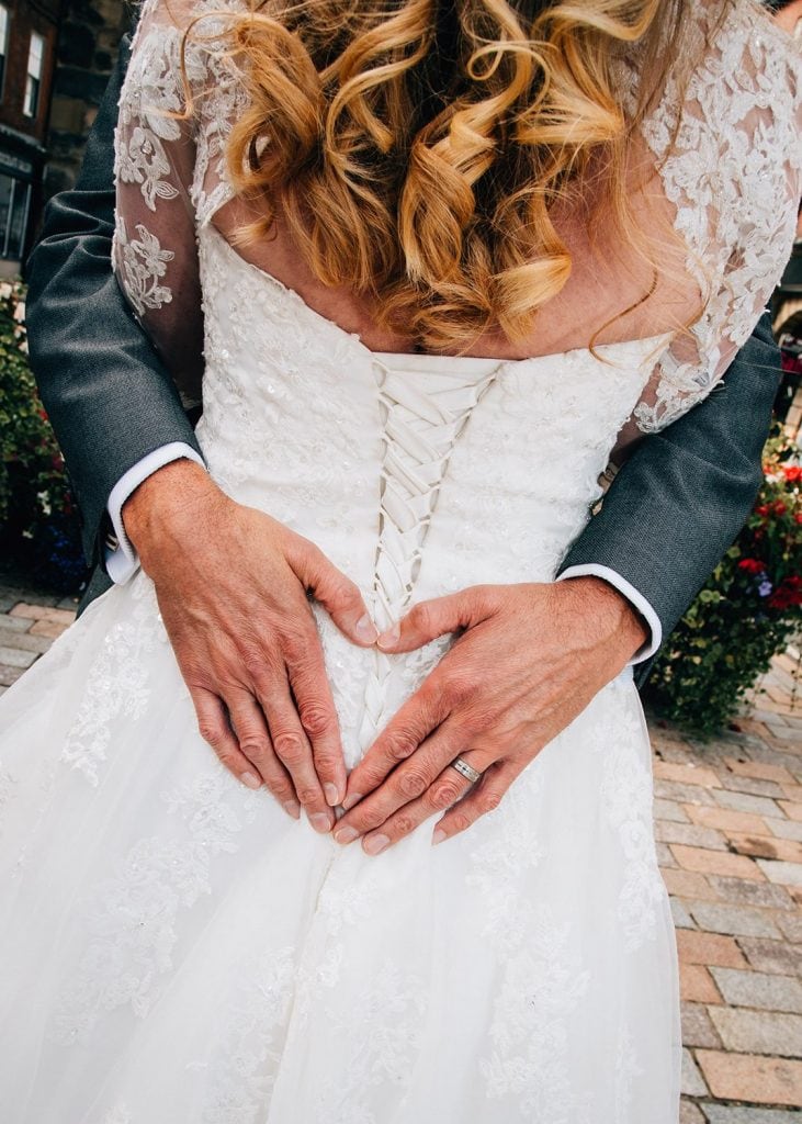 The grooms hands making a heart shape on his brides back