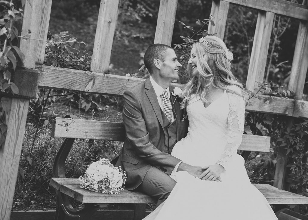 The bride and groom smiling on a bench at Carlisle Park in Morpeth, Northumberland