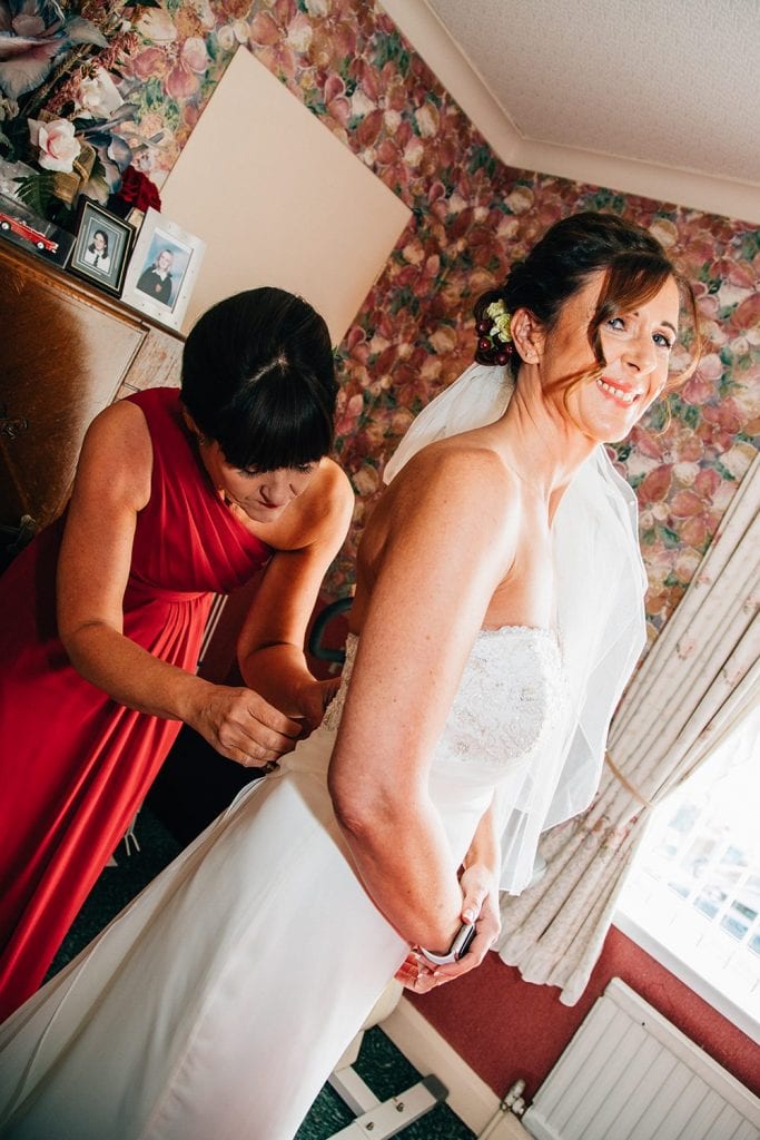 Bridesmaid helping the bride into her dress